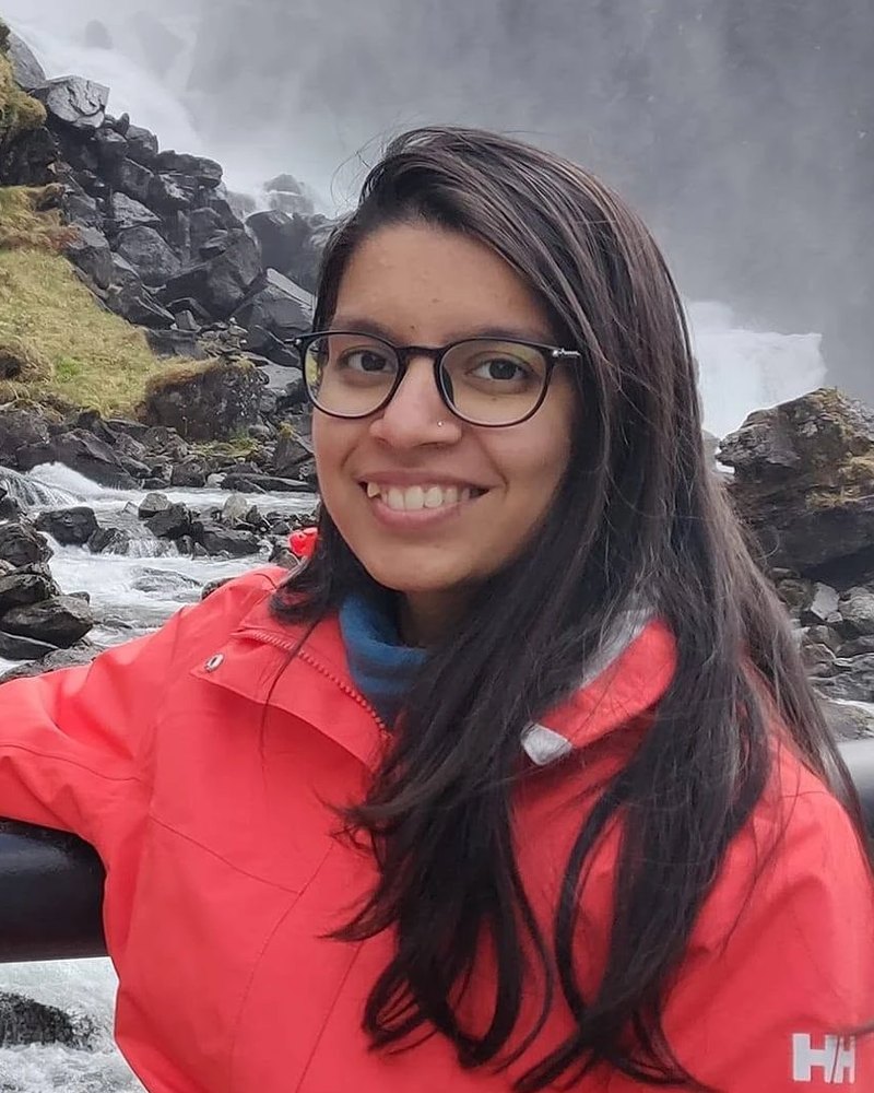 Sona smiler foran en foss, i rød regnjakke.